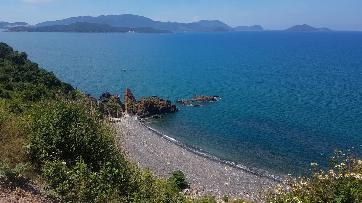 Rocky headland and a narrow shingle beach curving beside calm blue sea