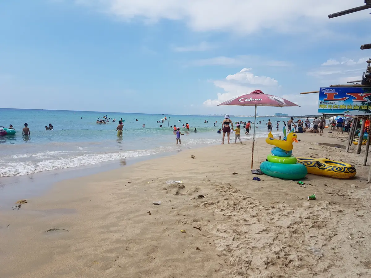 Swimmers in shallow water near a beach umbrella and an inflatable ring on pale sand