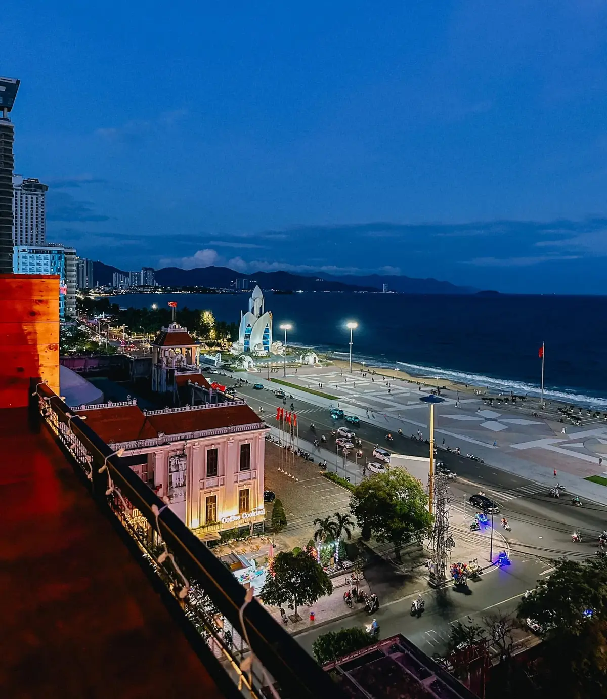 Evening view from a rooftop over a pink building, a square and the sea with a tower in the distance