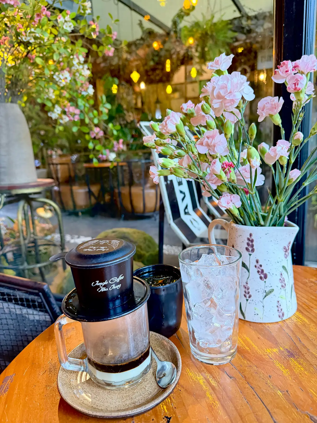 Vietnamese phin coffee filter and an iced glass beside a vase of pink flowers