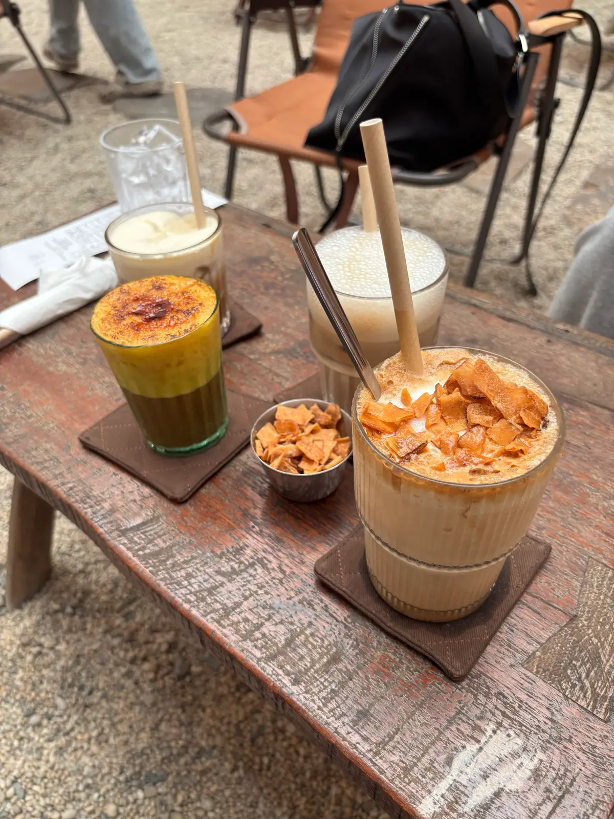 Iced coffee topped with coconut chips and a layered drink on a wooden table