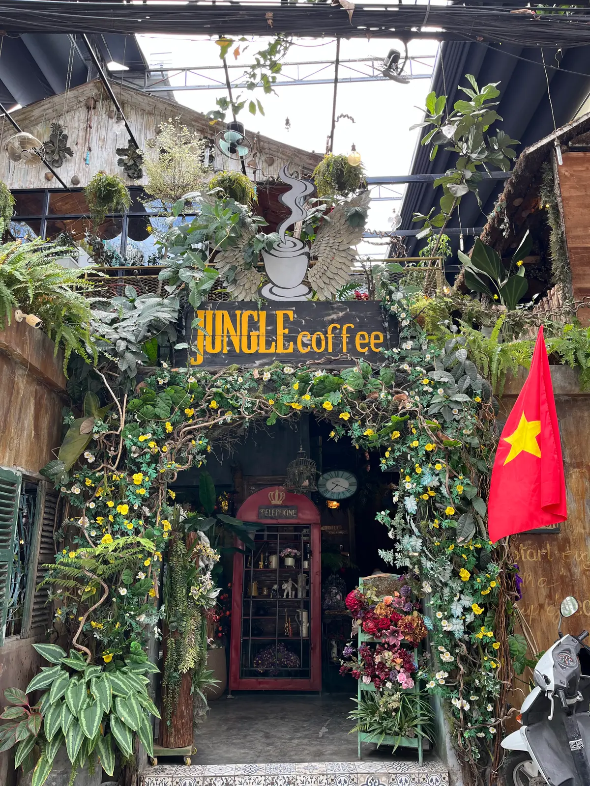 Wooden Jungle Coffee sign covered by vines and flowers above a red phone box