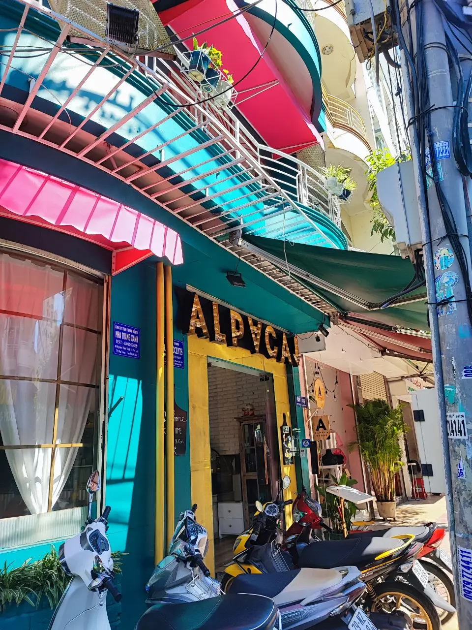 Teal corner cafe front with a yellow Alpaca sign and pink awning
