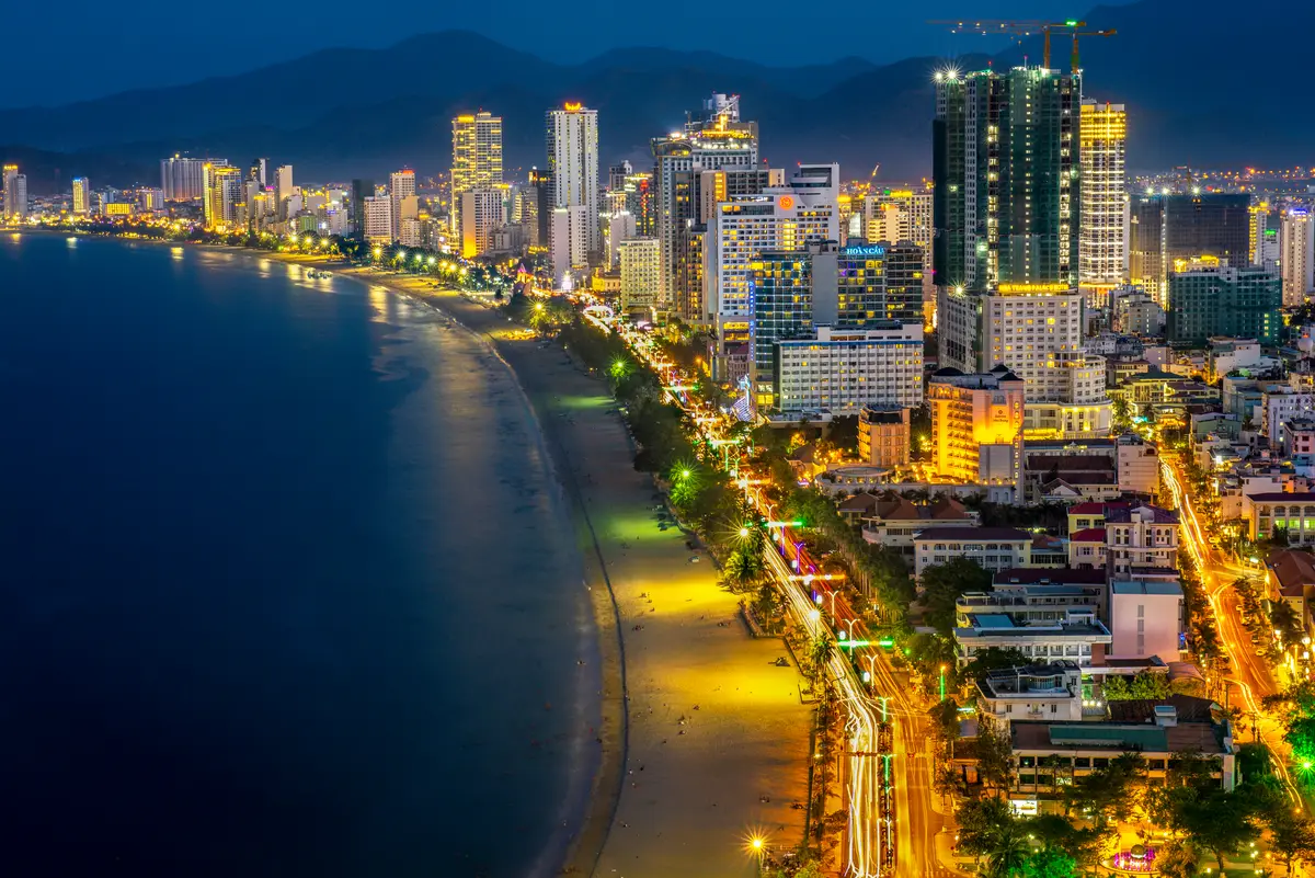 Nha Trang bay and the lit beach road at dusk, with hotel towers glowing along the curve of the shore