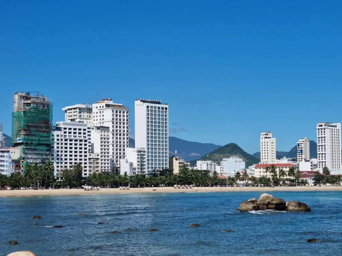 Nha Trang high-rise hotels along the waterfront on a clear day, with rocks in calm blue water in the foreground