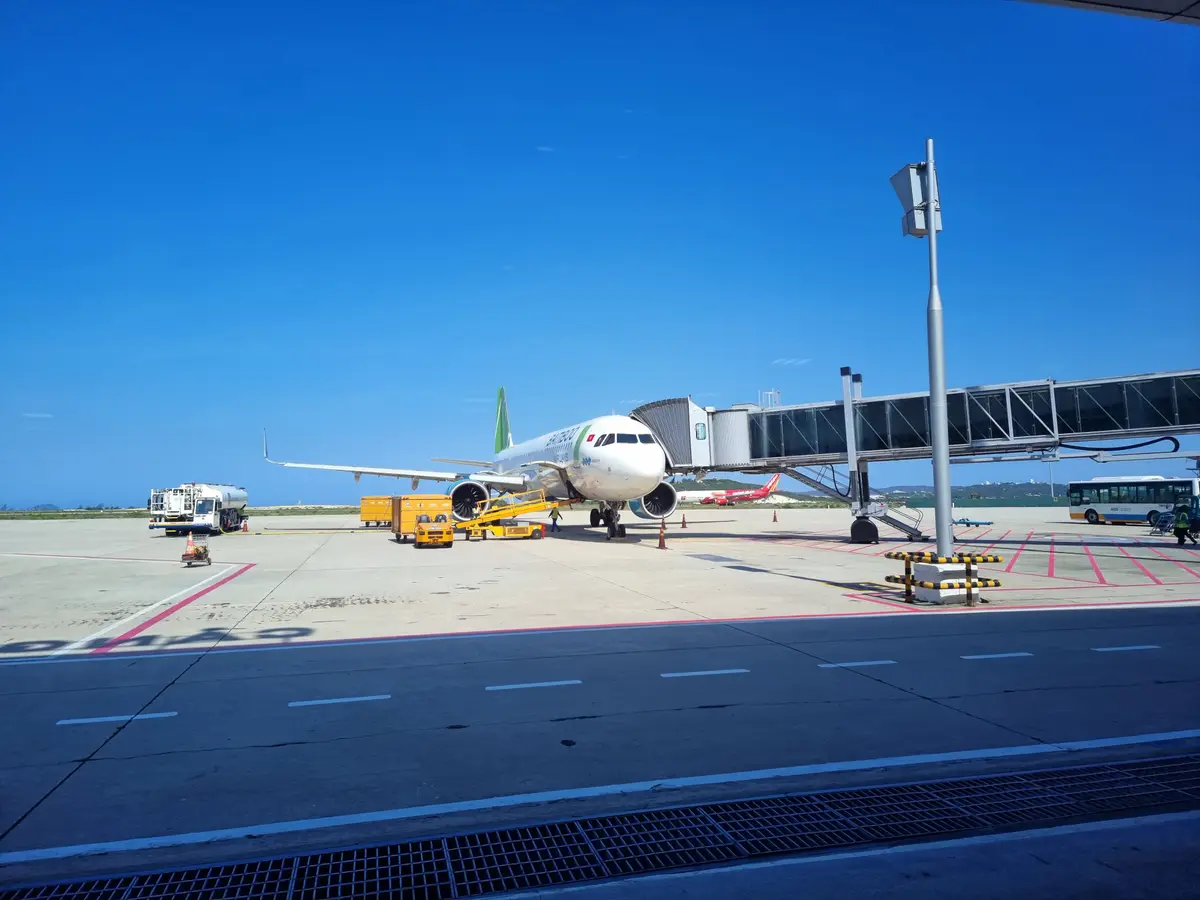 Passenger jet parked at a jet bridge on the apron under a blue sky.