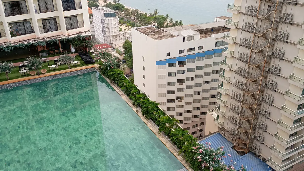 Turquoise swimming pool with a flower border beside a white apartment block seen from above