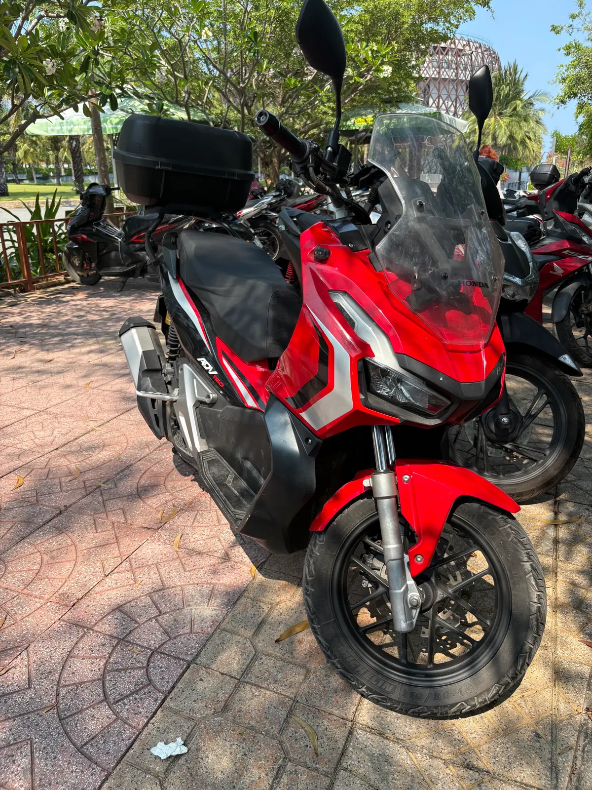 Red and black Honda ADV scooter parked on paving beside other bikes