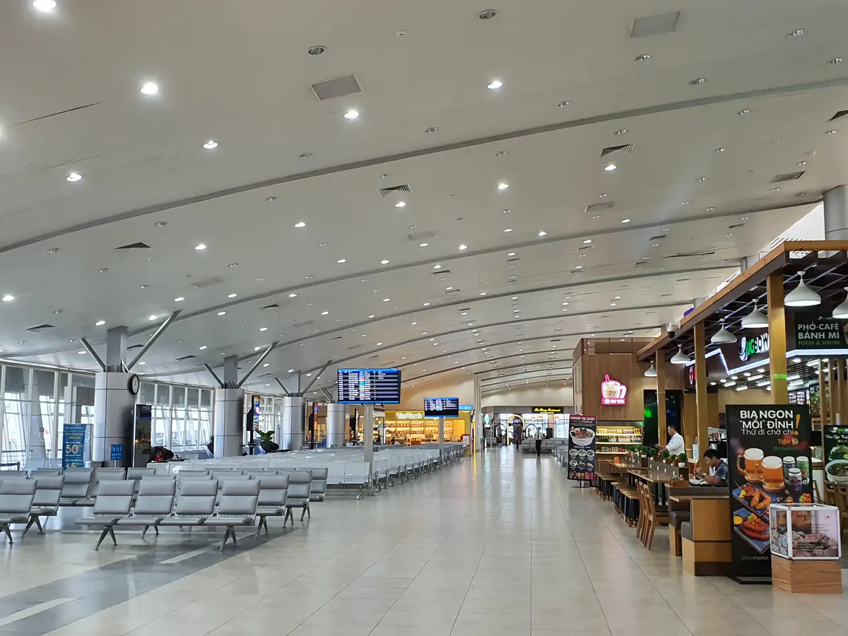 Wide departures and arrivals hall at Cam Ranh International Airport with rows of seats, a cafe and a high ceiling with bright lights
