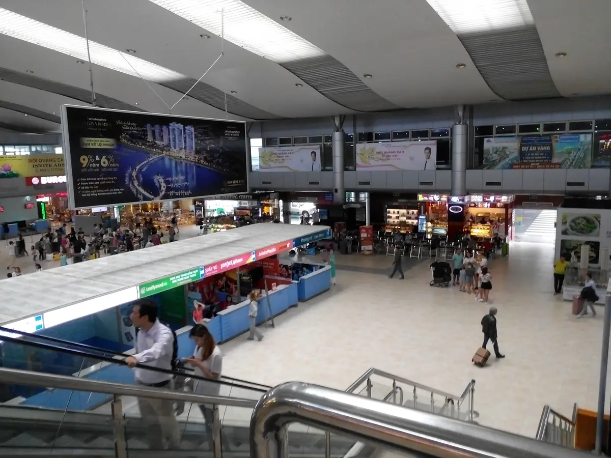 Busy arrivals hall at Cam Ranh International Airport seen from the escalator, with a long counter, signs and passengers with luggage