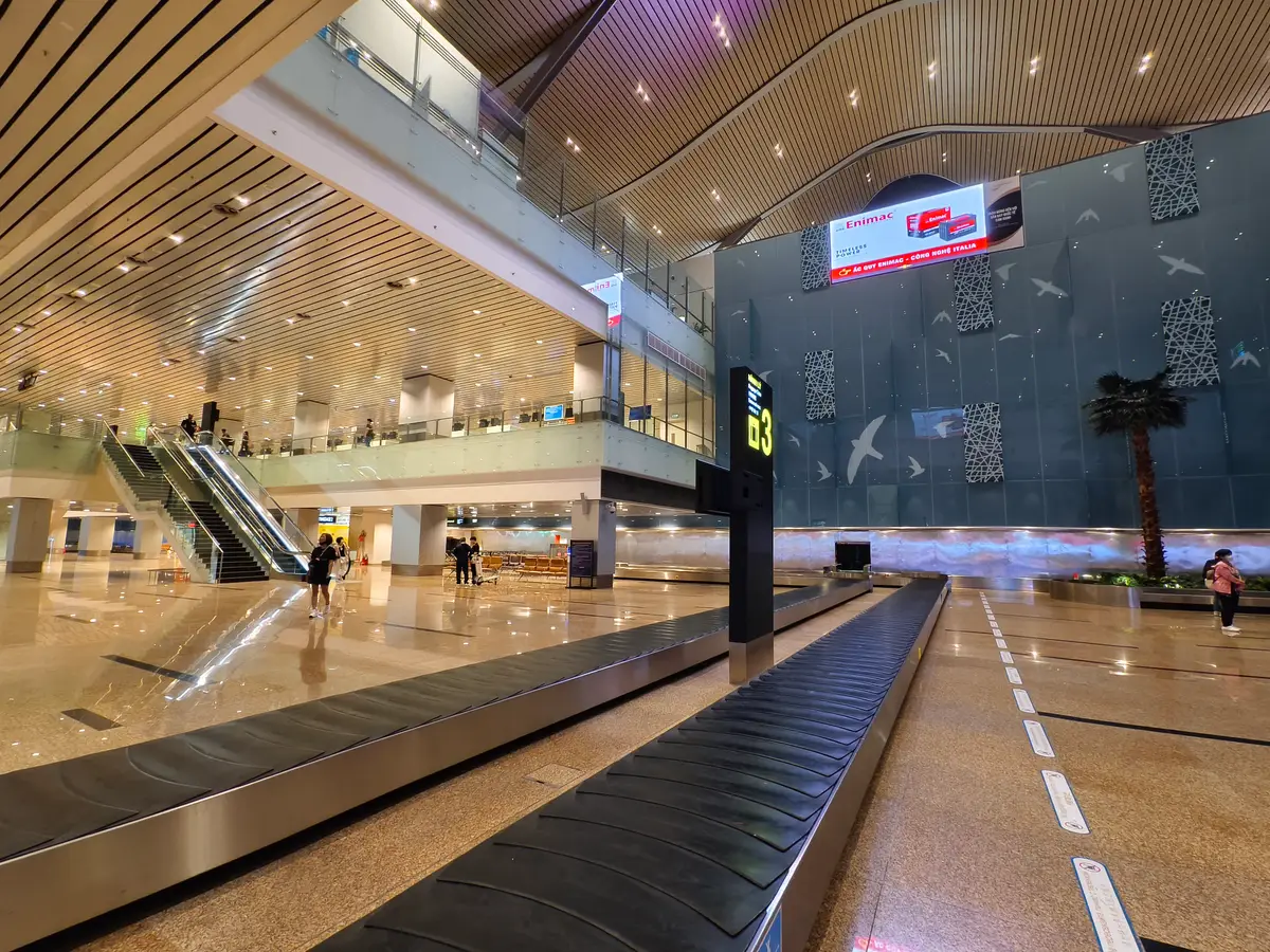 Baggage carousel in the arrivals hall at Cam Ranh International Airport with an escalator and a high wooden ceiling
