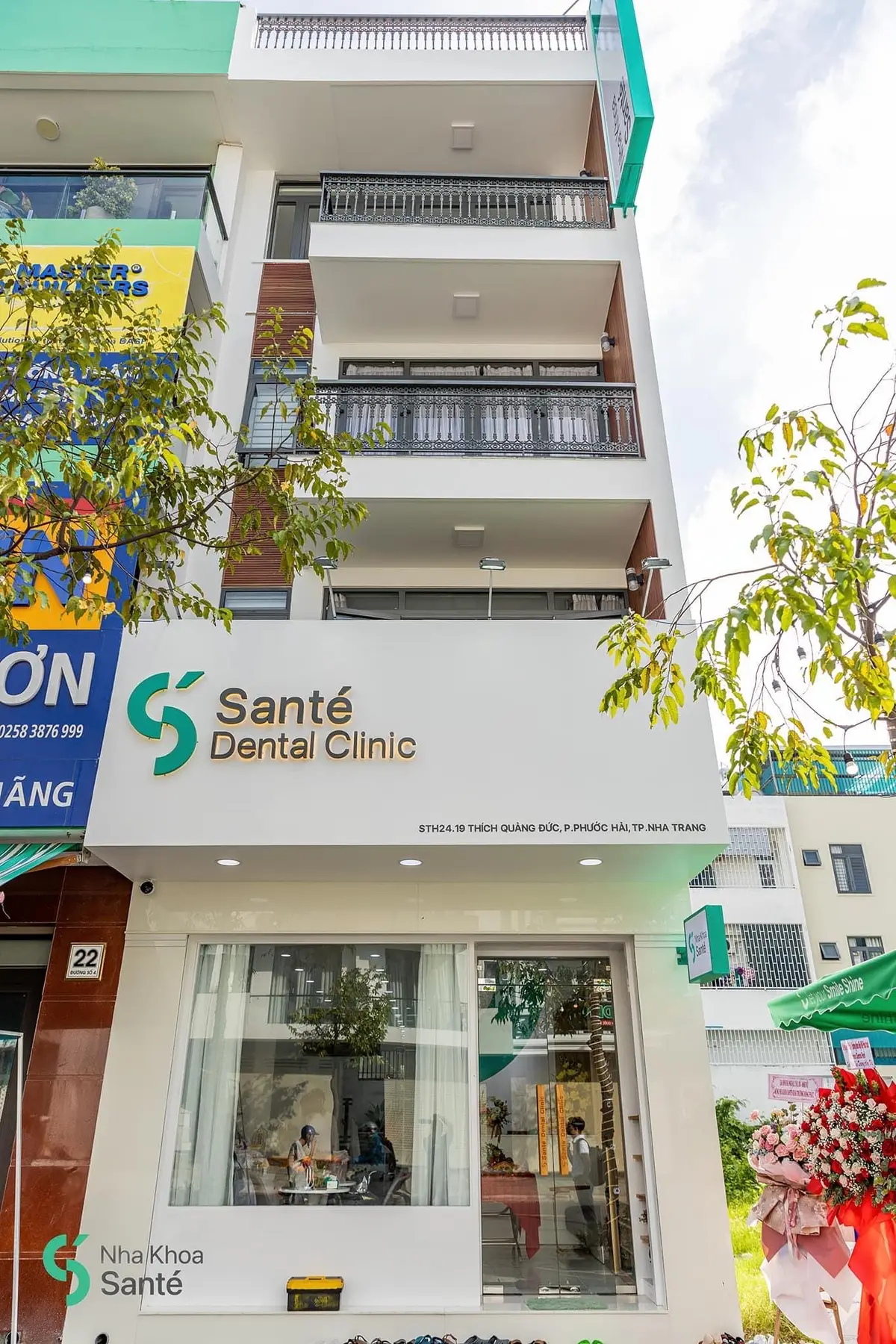 White two-storey dental clinic front with a Sante Dental Clinic sign and a tree