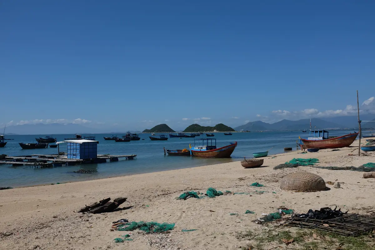 Small fishing boats and a blue hut on a sandy beach with islands in the distance