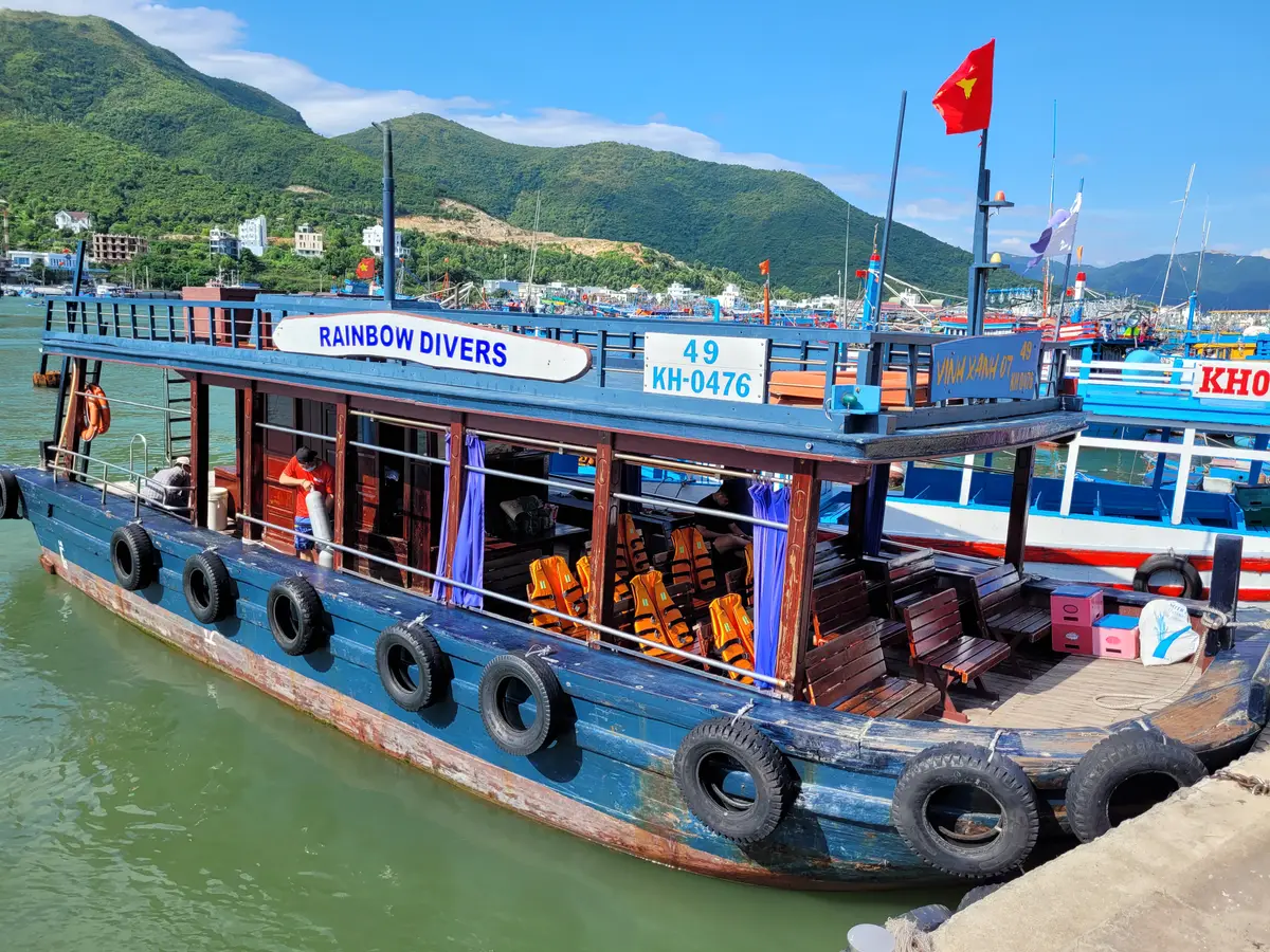 Blue wooden dive boat with a Rainbow Divers sign and passengers in orange life jackets