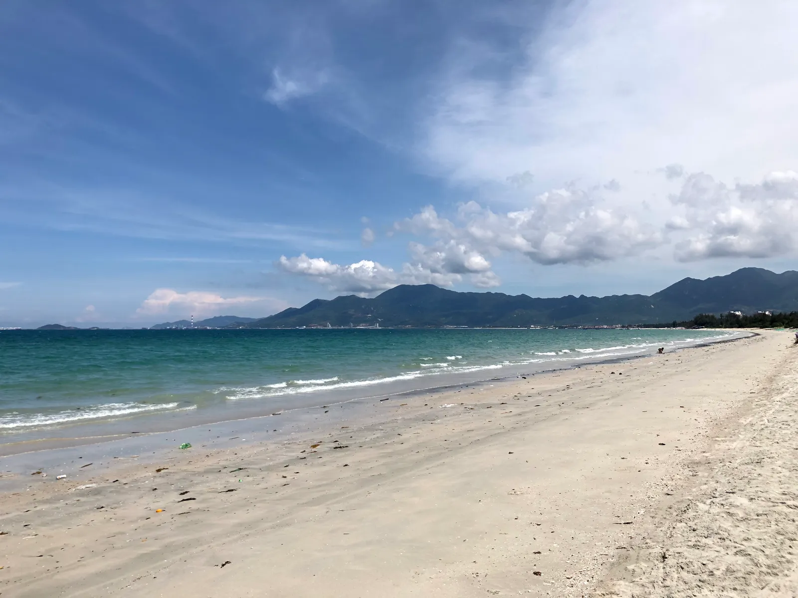 Long empty sandy shoreline under a blue sky with distant hills