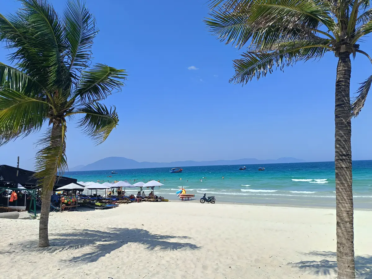 White sand beach with palm shadows, small boats and a distant headland