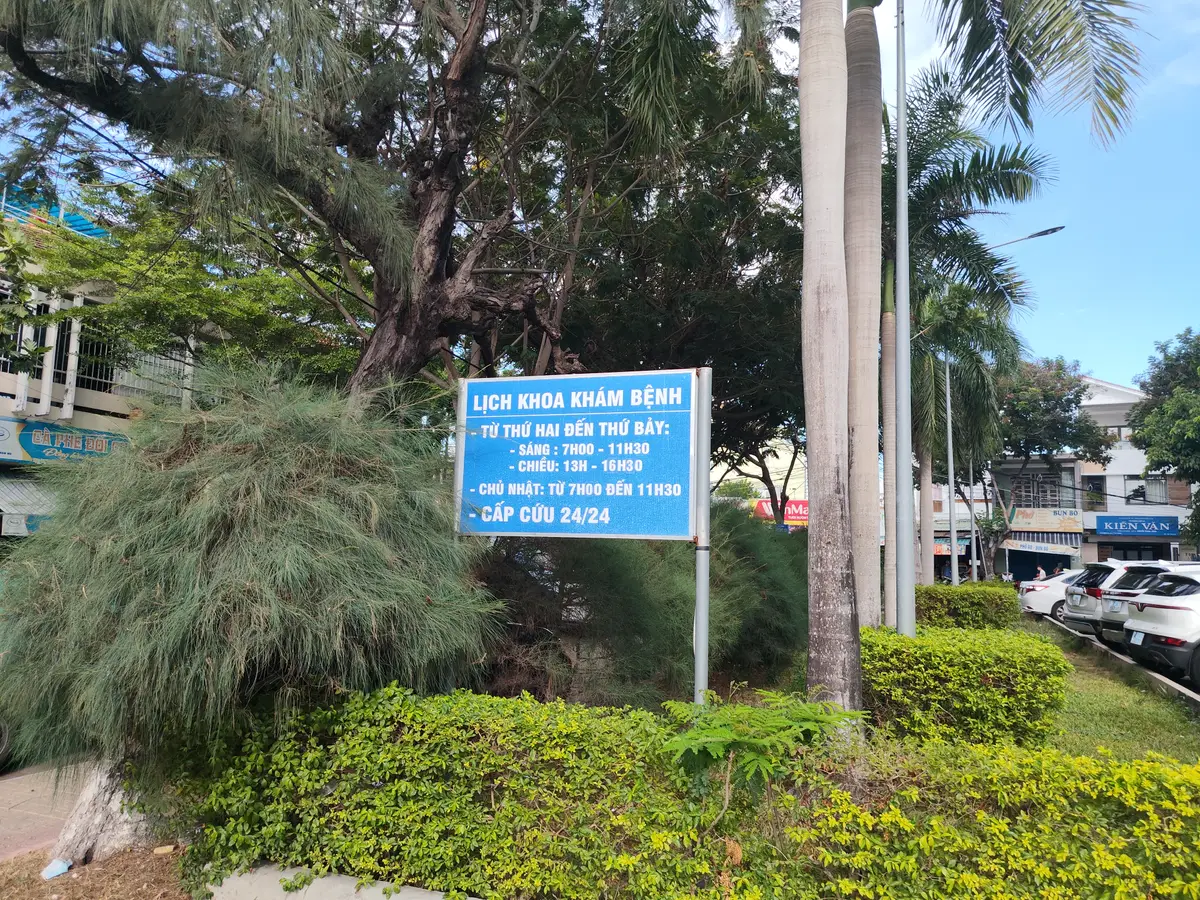Blue roadside sign with the outpatient schedule beside a garden