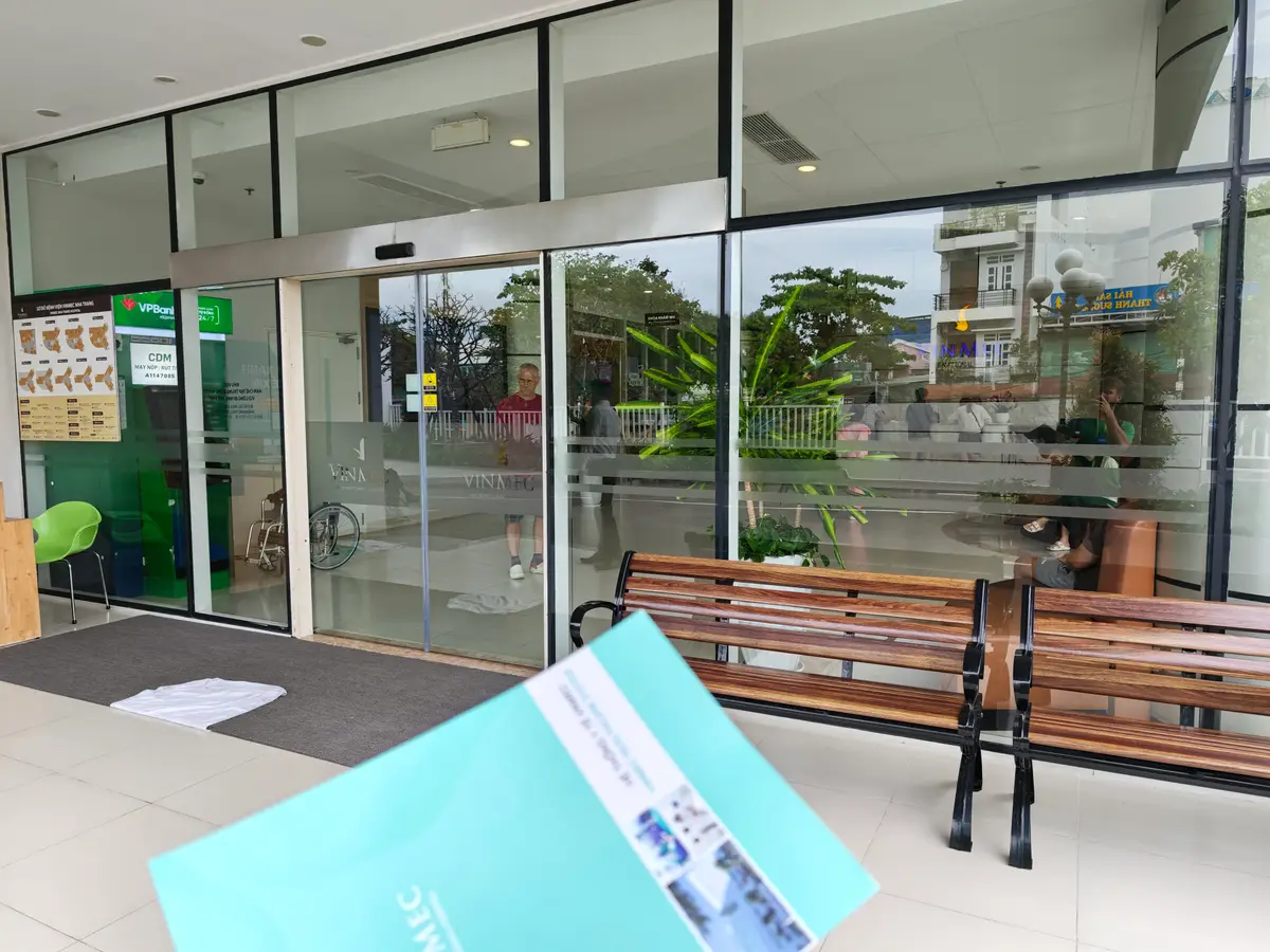 Hospital lobby with wooden benches beside glass doors and a leaflet on the bench