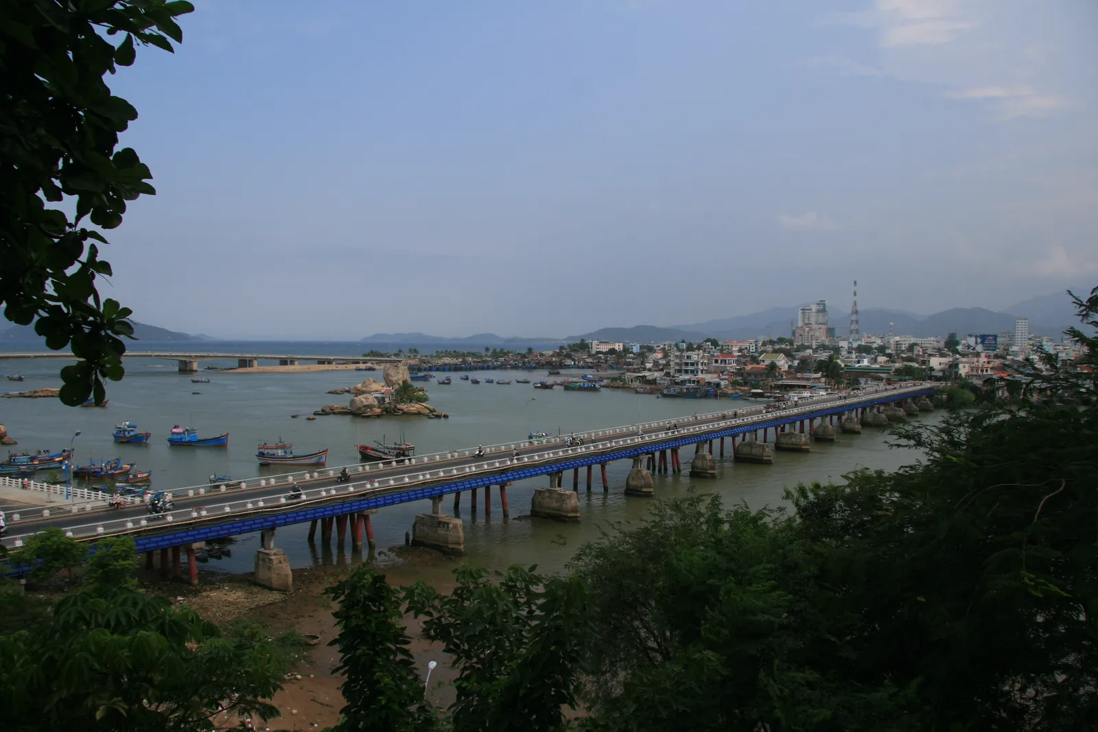 Long road bridge over a wide river with the Nha Trang riverside and hills in the distance