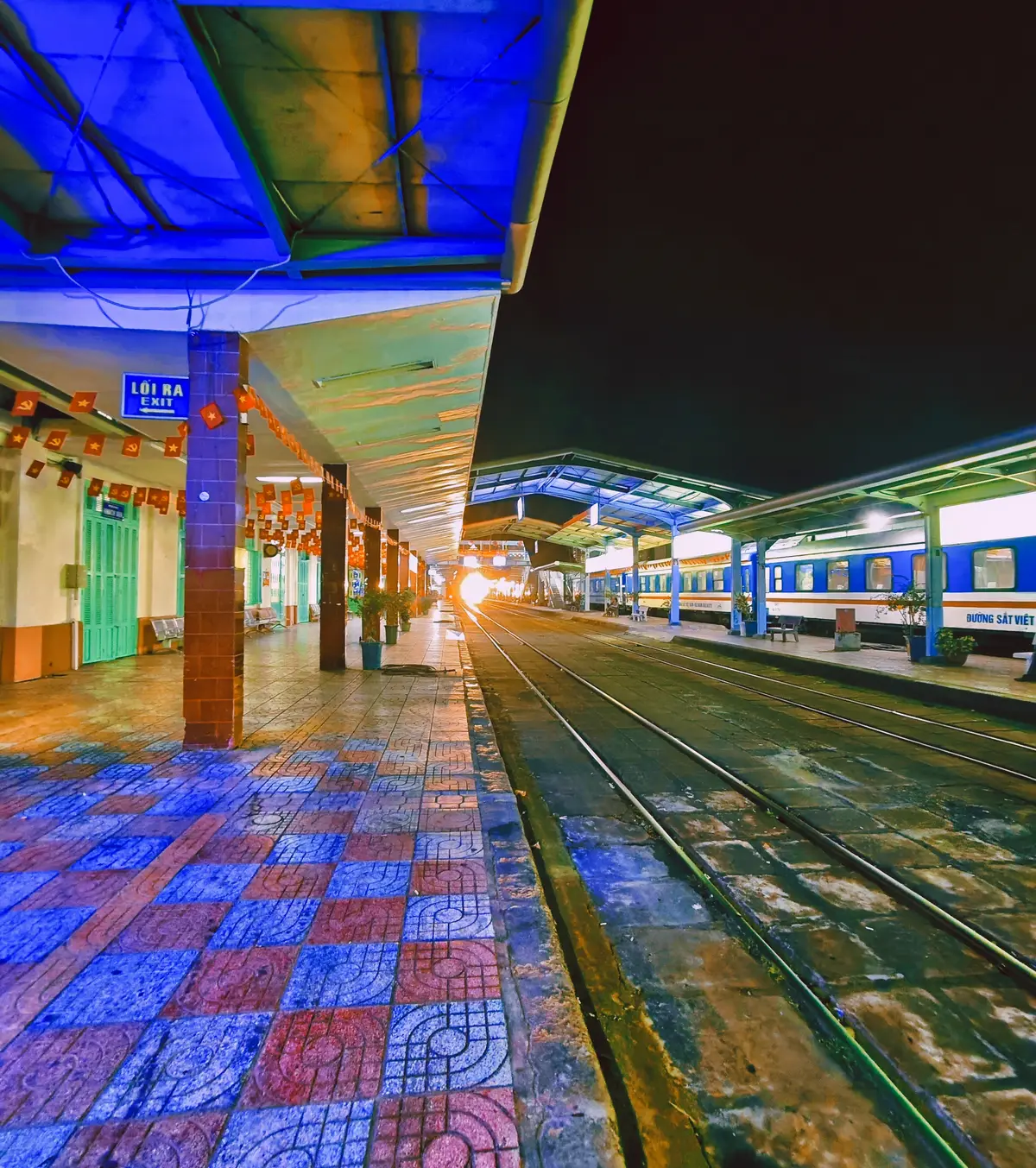 Covered platform at Nha Trang railway station with blue columns, colourful tiles and a train alongside