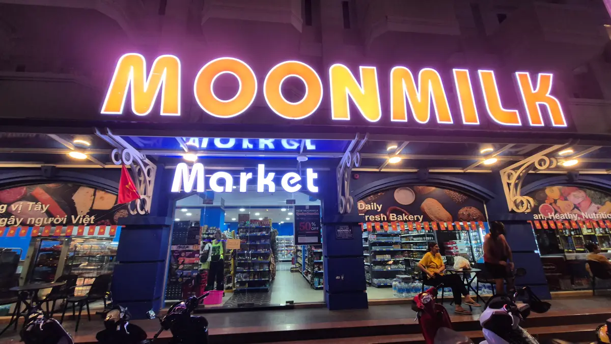 Shopfront at night with a lit Moonmilk Market sign and a bakery shelf visible inside