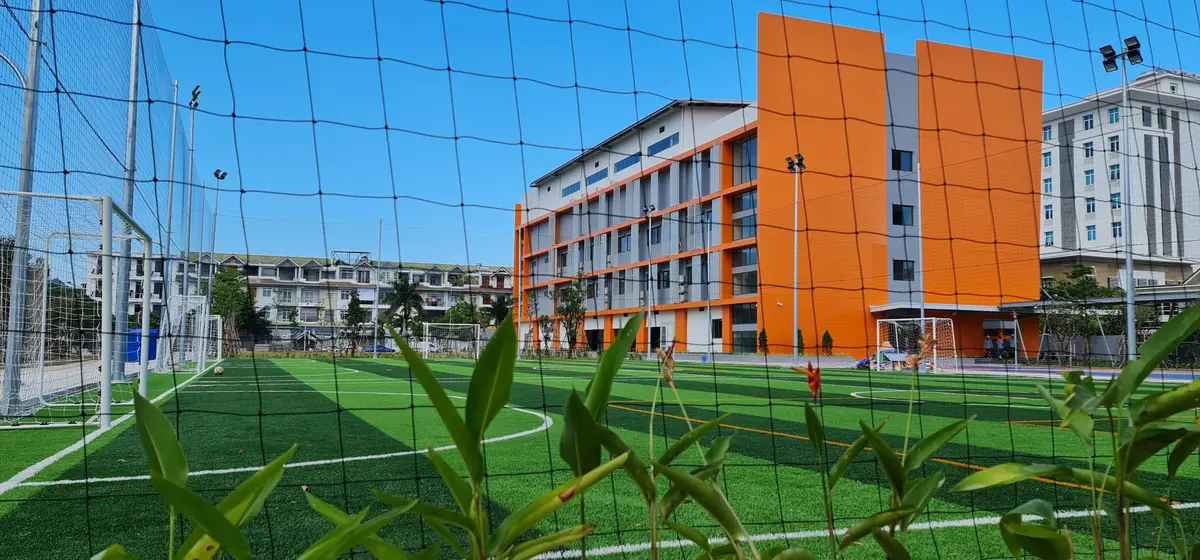 Green sports pitch behind a net with the orange school block in the background