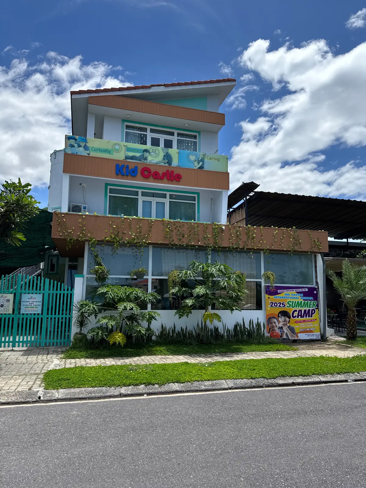 A two-storey building with a Kid Castle sign above a landscaped front garden and a green fence.