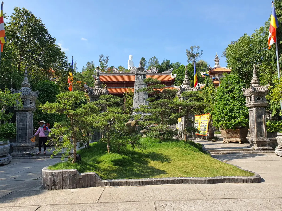 Trimmed pine and lawn in a pagoda garden with temple roofs and prayer flags beyond