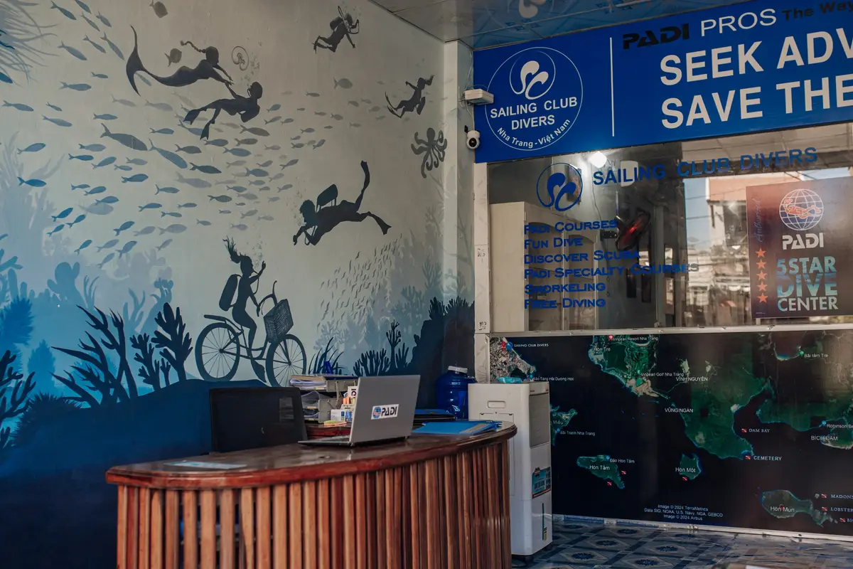 Dive shop reception desk with a laptop, a wall painted with divers and fish, and a map of dive sites