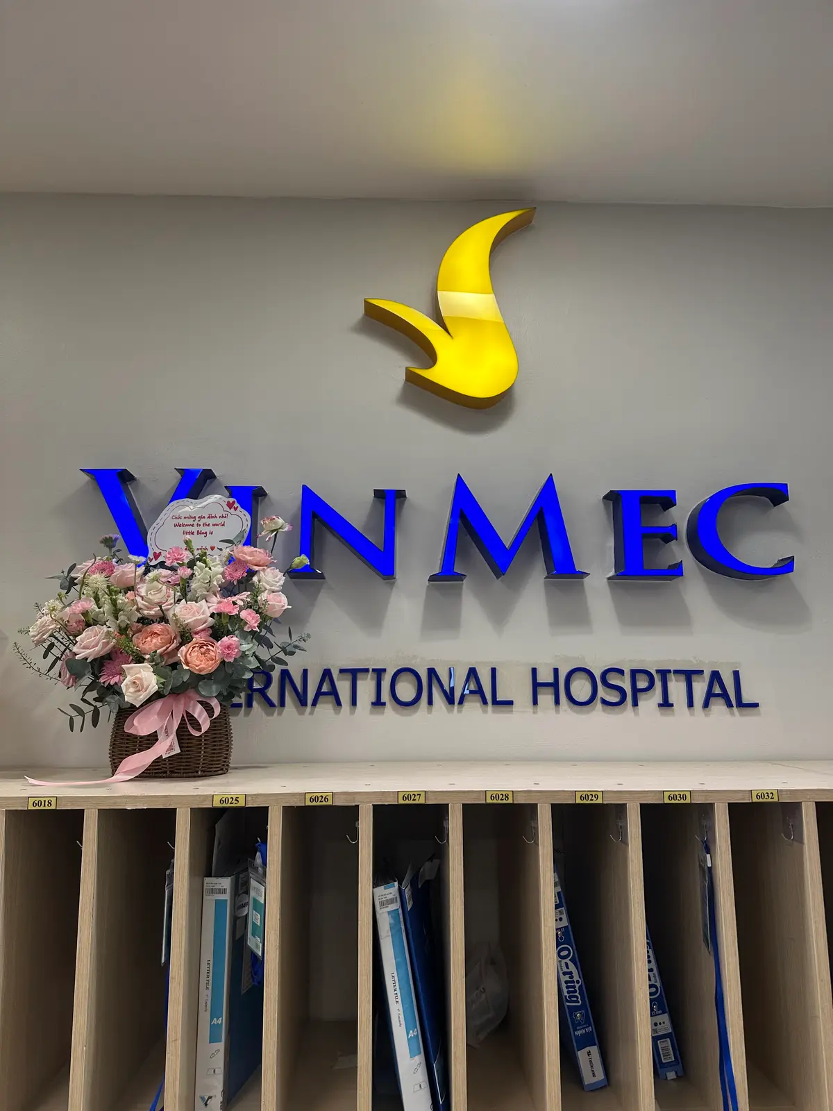 Blue hospital logo above a flower arrangement on a wall