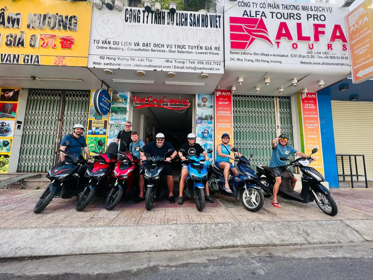 Row of scooters parked in front of a travel agency shopfront with a group of riders sitting on them