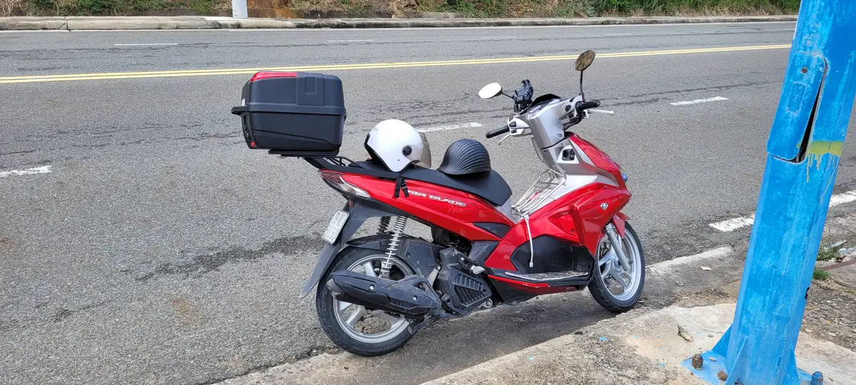 Red and silver scooter with a black top box and a white helmet on the seat, parked on an empty road