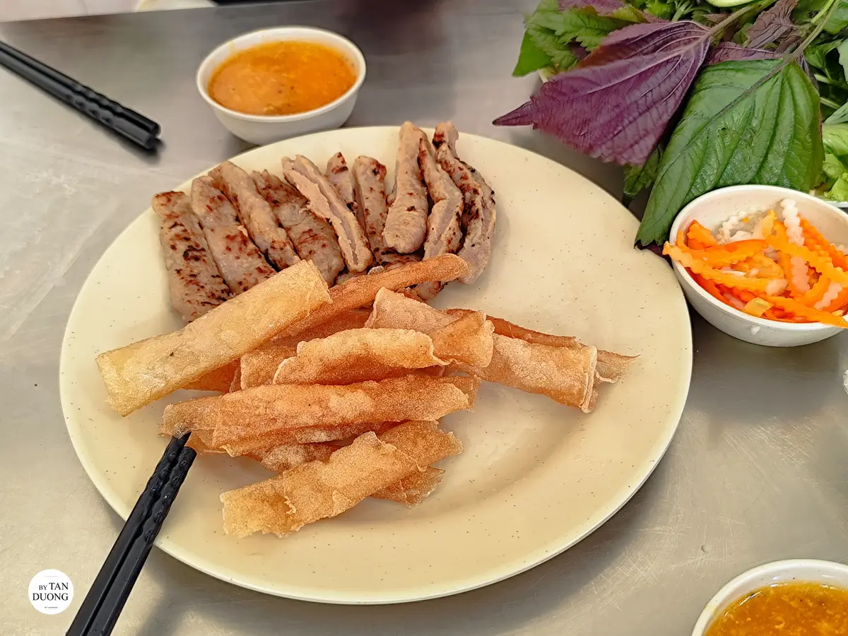 Round plate of sliced grilled pork rolls and fried rice paper rolls with herbs and dipping sauce