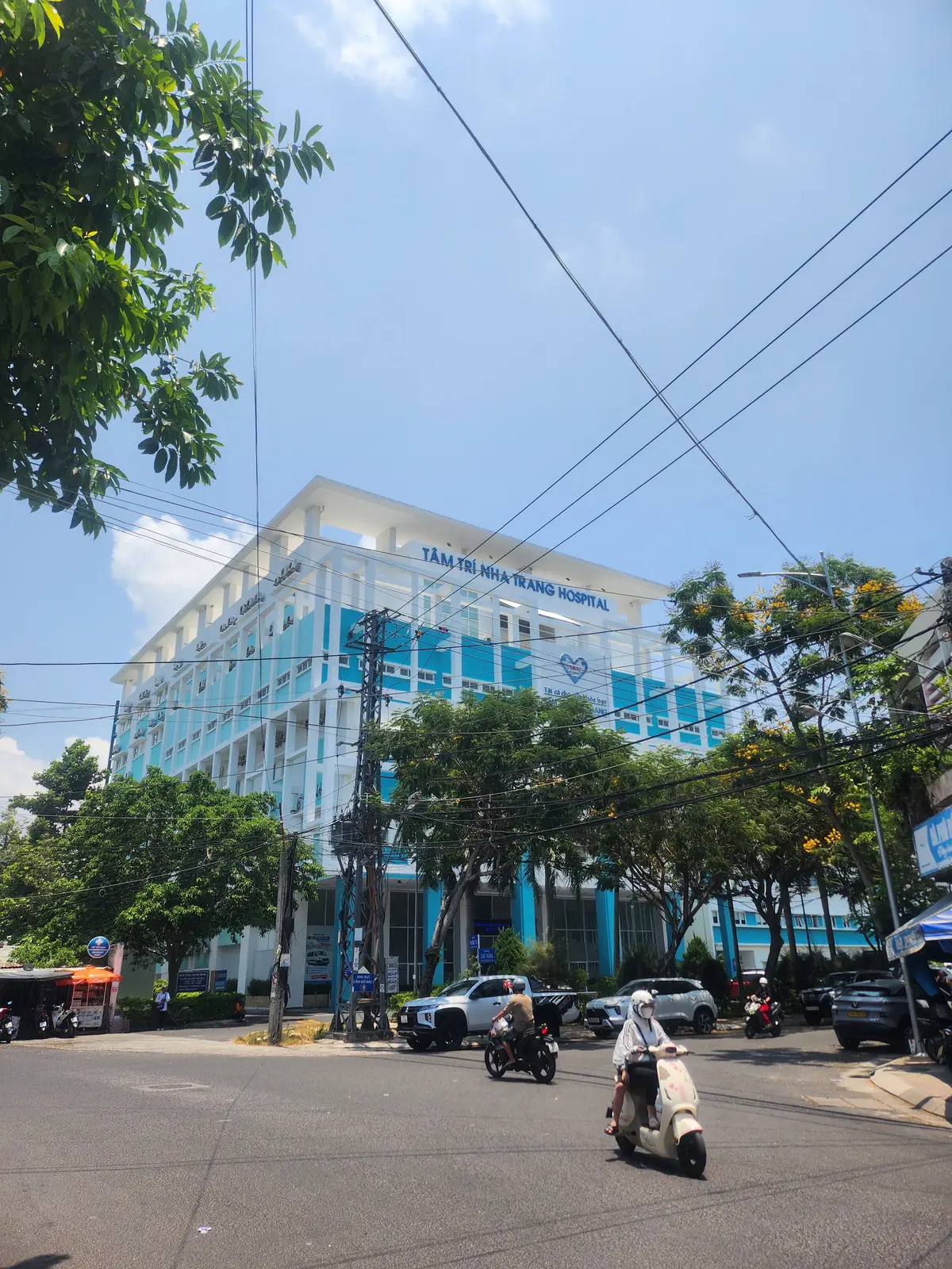 Five-storey white and blue Tam Tri Nha Trang General Hospital building seen from the street, with trees in front