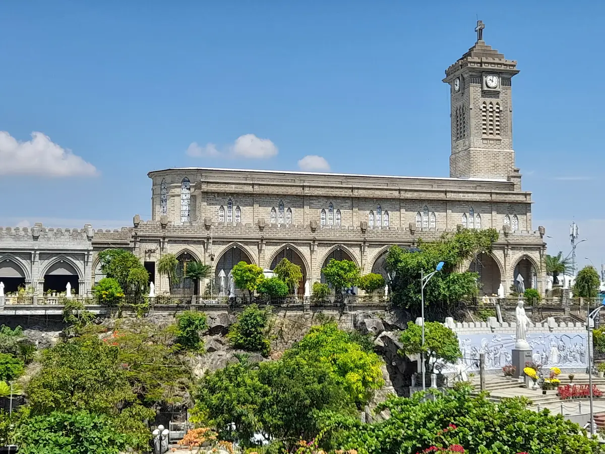 Grey stone cathedral and bell tower on its hill above gardens and a white shrine