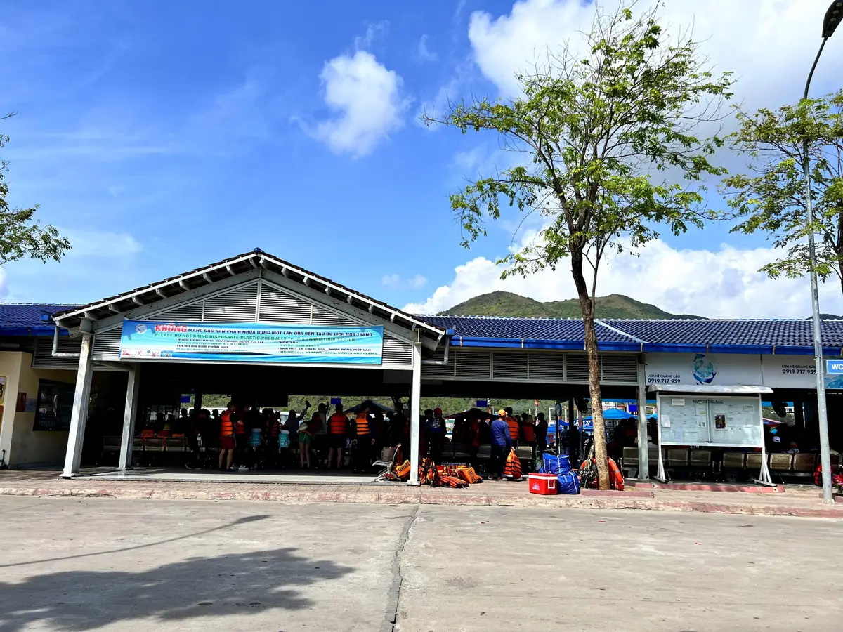 Low ticket hall with a blue roof and a crowd waiting in life jackets at the pier