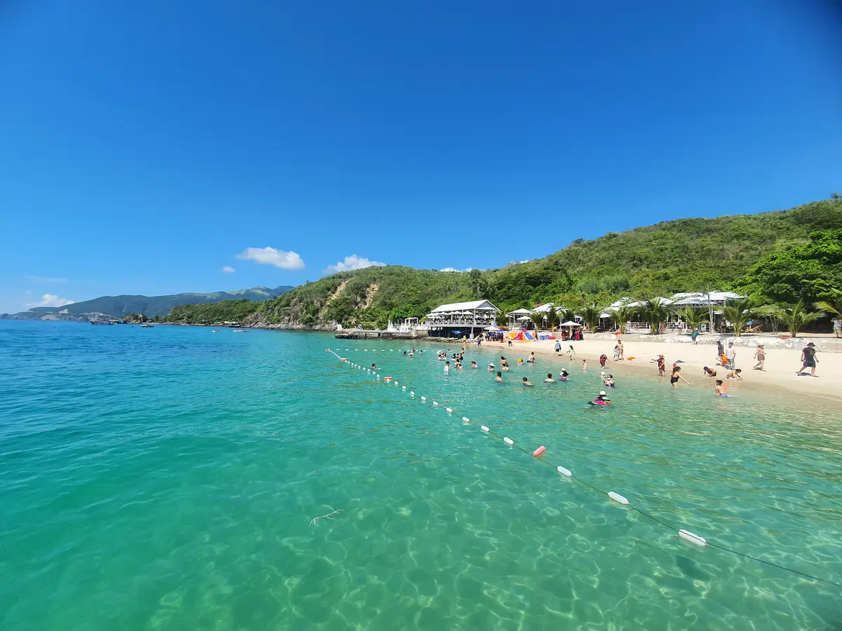 Bright turquoise water with a line of buoys marking a swimming area and a hillside beach