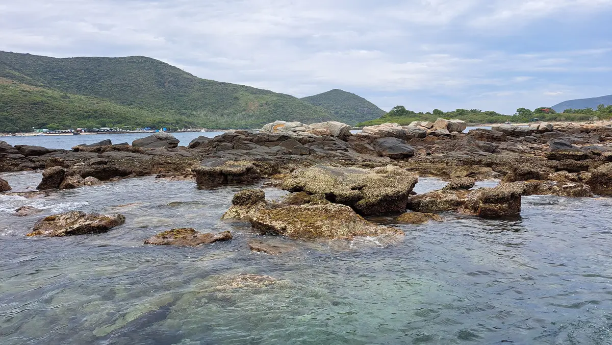 Flat dark rocks along the shore with green hills behind