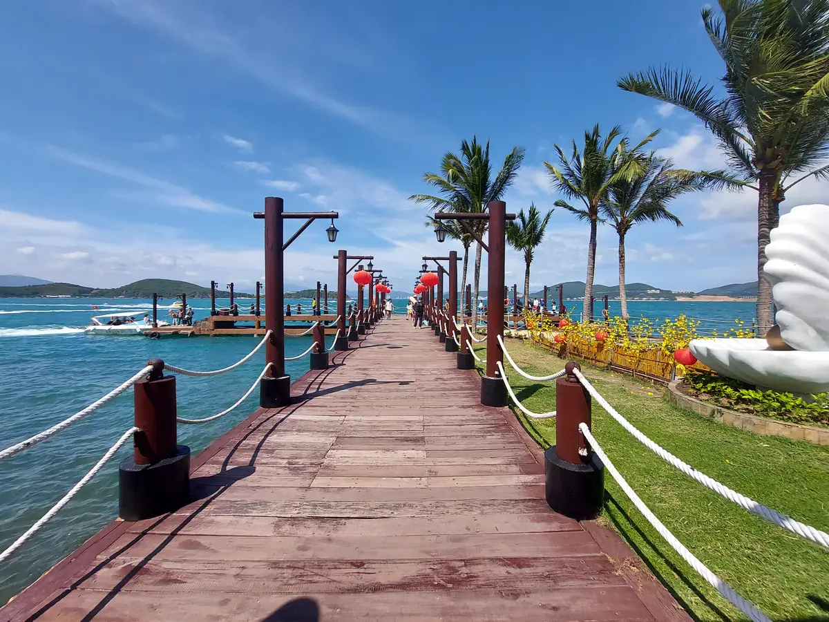 Wooden jetty with red posts running out over the sea toward palm trees