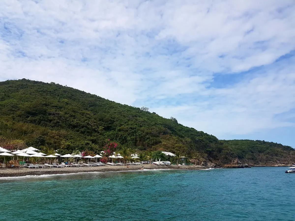 Rows of white parasols along a narrow beach below a green hillside