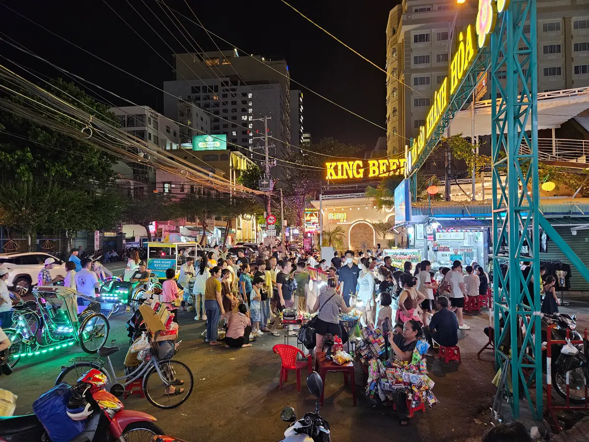 Crowded night street with neon lights and lit pedicabs