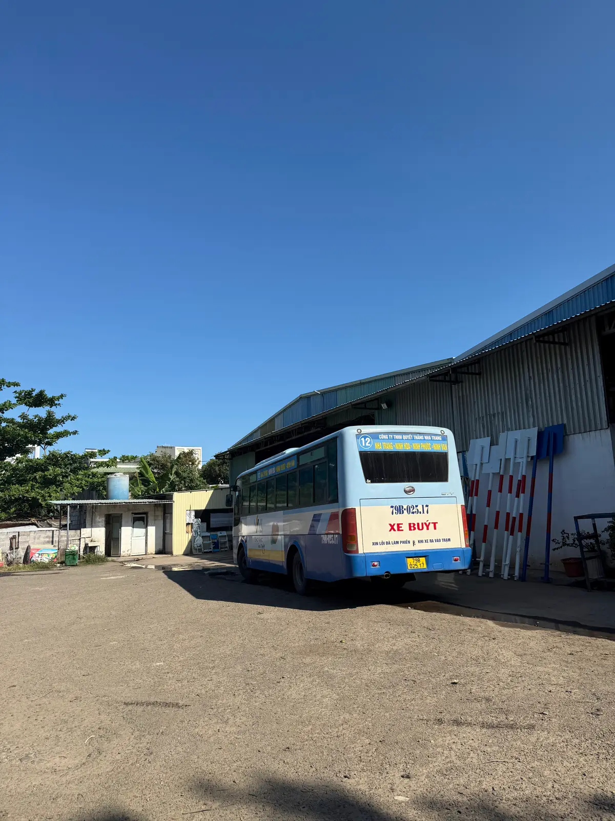 Blue and white city bus beside a depot building with a metal roof in Nha Trang