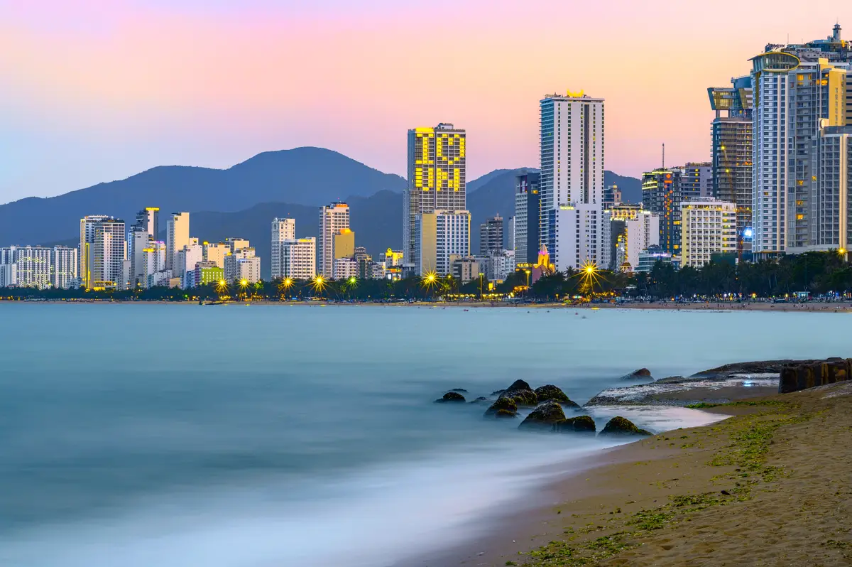 Rocky shore and calm silky water at Nha Trang at dusk with the city skyline and mountains behind