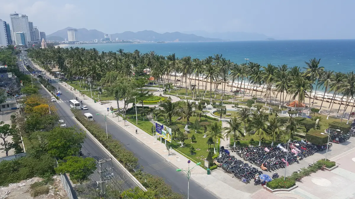 Aerial view of the Nha Trang coastal road and palm-lined promenade beside the sea with mountains in the distance