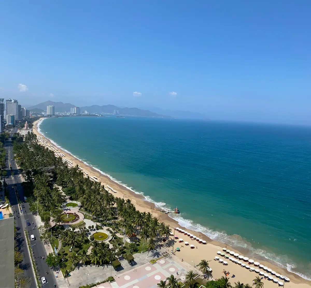 Deep blue sea and the long curve of Nha Trang beach seen from above, with the city and mountains behind