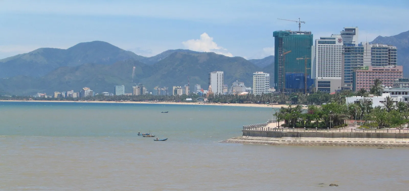 Nha Trang seafront with a long beach, high-rise buildings, a calm bay with small boats and mountains behind the city