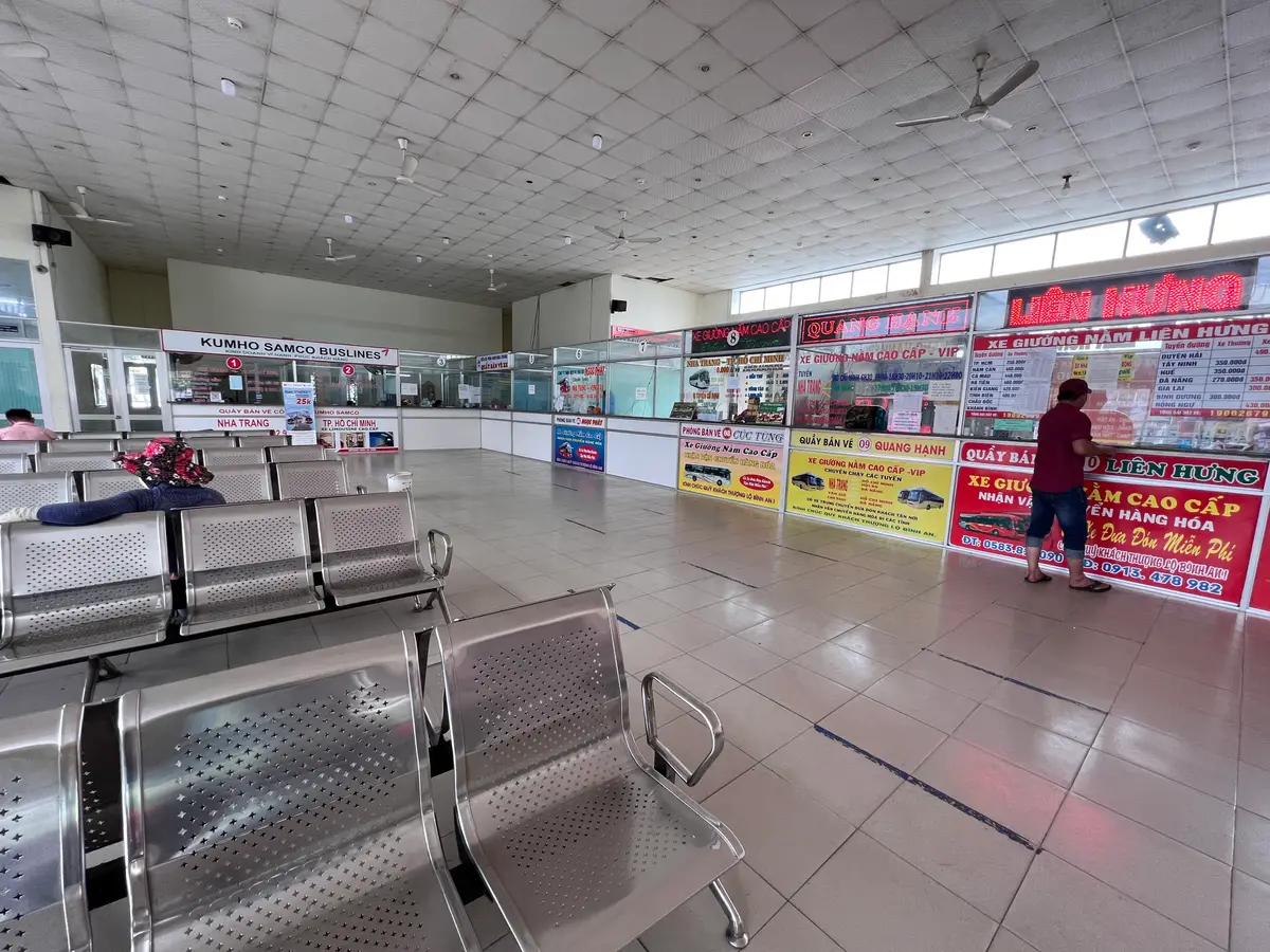 Large bright waiting hall with rows of metal seats and ticket counters along the far wall