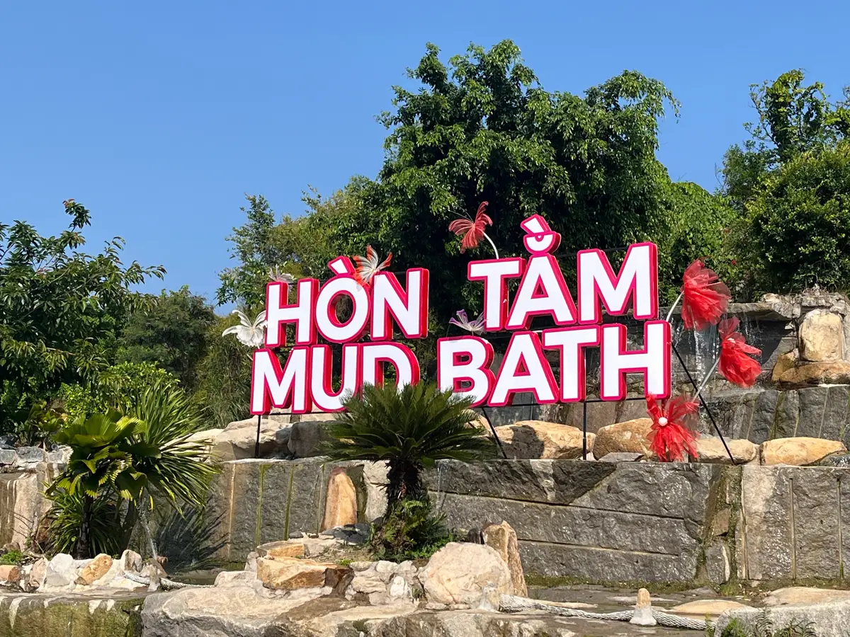 Pink illuminated Hon Tam Mud Bath sign among rocks and shrubs