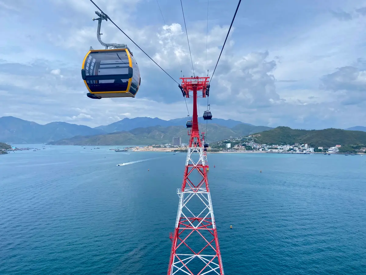 Cable car cabin hanging from a red steel tower above the bay with mountains behind
