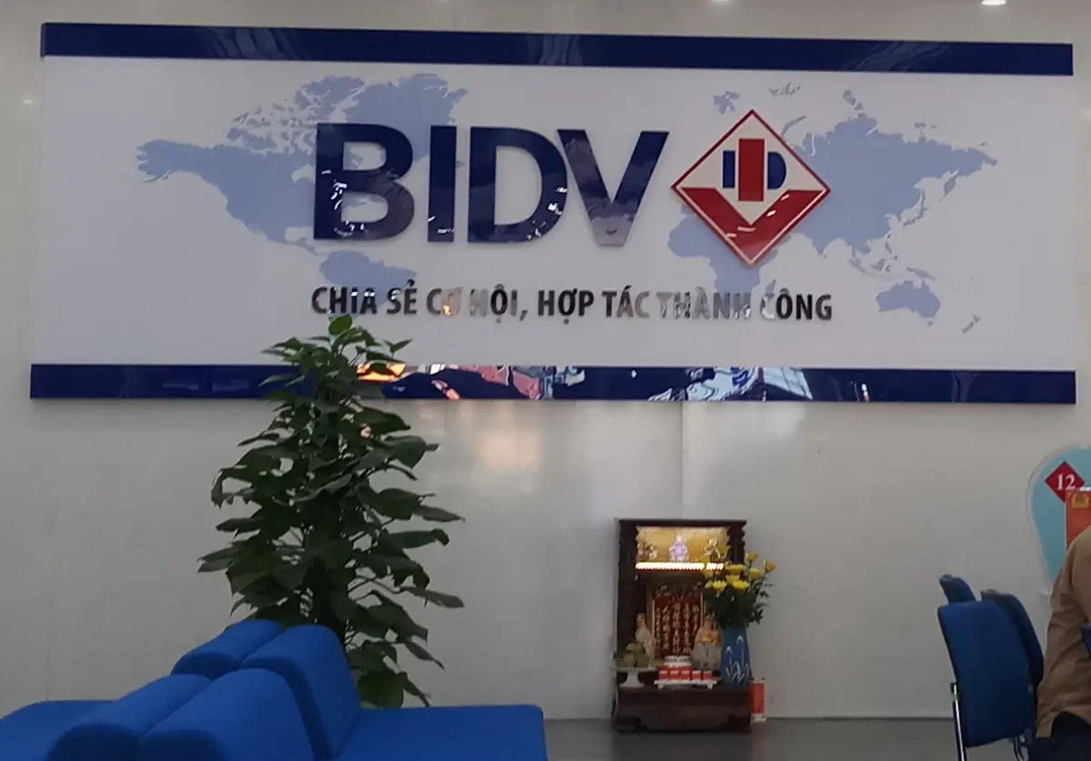 Branch hall wall with the BIDV logo over a world map, a blue waiting sofa and a plant in front